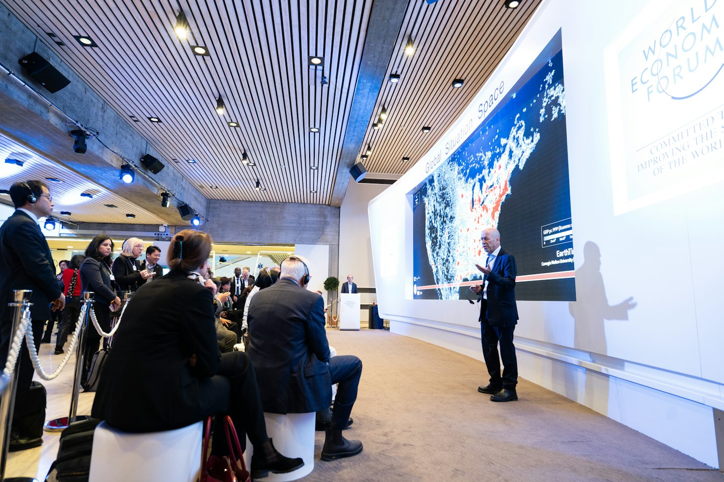 Un uomo presenta una mappa di dati su uno schermo curvo a un pubblico in conferenza.